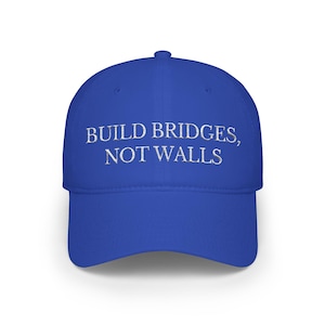 May include: A royal blue baseball cap featuring the embroidered phrase "BUILD BRIDGES, NOT WALLS" in white. The cap has a curved peak and a structured crown. This hat is a stylish accessory for everyday wear.