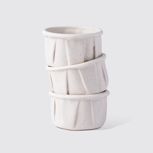 May include: A set of three ceramic mugs with a speckled, matte finish. The mugs are in shades of blue, green, and white. Each mug has a simple, modern design, perfect for coffee or tea.