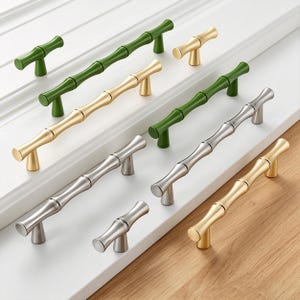 May include: A collection of bamboo-style cabinet pulls in various colors. The pulls are in green, gold, and silver, with a bamboo stalk design. The hardware is displayed on a white surface and a wooden surface.