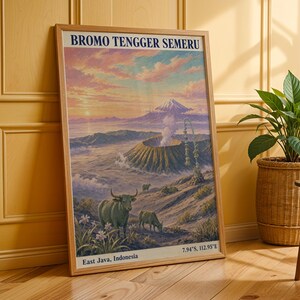 Può includere: Un poster da viaggio verticale incorniciato intitolato BROMO TENGGER SEMERU che presenta un'illustrazione paesaggistica di un cratere vulcanico, una montagna fumante e bestiame al pascolo a Giava Orientale, Indonesia, con le coordinate 7.94°S, 112.95°E in basso.