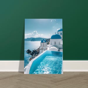 May include: A framed print of a scenic coastal view. The image features white buildings with blue domes, a turquoise pool, and the Aegean Sea under a bright blue sky. The print is leaning against a dark green wall.
