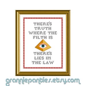 May include: A gold framed cross-stitch with red and white borders. The cross-stitch features a pyramid with an eye inside and the text "There's truth where the filth is. There's lies in the law."