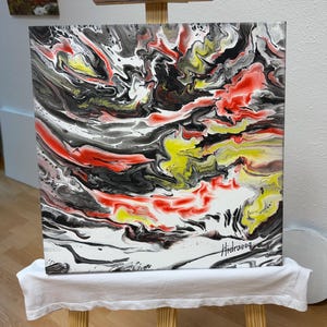 Könnte beinhalten: Abstrakte Acrylmalerei auf Leinwand, präsentiert auf einer hölzernen Staffelei. Das Kunstwerk zeigt ein fließendes Design mit wirbelnden Mustern in Rot, Schwarz, Weiß und Gelb. Die Signatur des Künstlers, "Hidraeoq", ist unten rechts sichtbar.