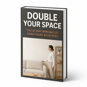 May include: A hardcover book titled "DOUBLE YOUR SPACE" with the subtitle "THE 21-DAY MINIMALIST SANCTUARY BLUEPRINT." The cover features a minimalist interior scene with a person standing near a sofa. The book has a black spine and a white background.