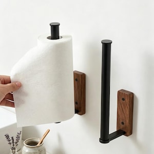 May include: Two wall-mounted holders featuring a matte black metal rod and a rectangular wooden base with visible grain. One holder supports a roll of white paper towels, while the other is empty, showcasing the vertical black metal design.