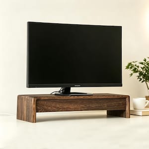 Könnte beinhalten: Ein dunkelbrauner Monitorständer aus Holz mit geschwungenem Design und einer Frontschublade, auf dem ein schwarzer Philips-Computermonitor steht. Der Ständer weist eine sichtbare Holzmaserung auf und steht auf einer ebenen Fläche.