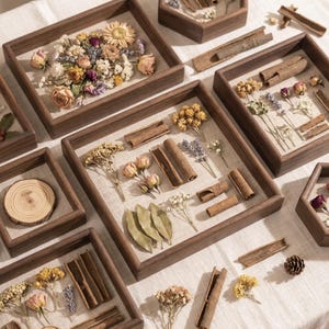 Peut inclure: Une collection de cadres de présentation en bois carrés et hexagonaux contenant des arrangements de fleurs séchées, de bâtons de cannelle, de feuilles de laurier et de tranches de bois. Les cadres ont une finition en bois naturel et un fond en tissu clair.