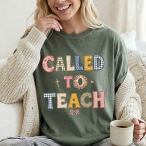 Może przedstawiać: Oliwkowozielony T-shirt z krótkim rękawem z napisem CALLED TO TEACH wykonanym czcionką w różne wzory. Litery zawierają motywy kwiatowe, kratkę vichy i kropki w odcieniach różu, żółci, błękitu i bieli, z małym krzyżykiem i kokardką.