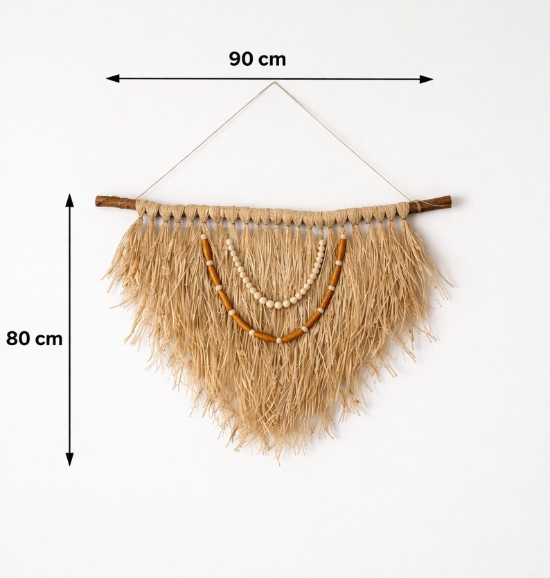 K&ouml;nnte beinhalten: Ein Wandbehang aus Naturfasern, 90 cm breit und 80 cm lang, mit einem Holzd&uuml;bel und dekorativen Holzperlen. Der beigefarbene Fransenbehang h&auml;ngt in einer dreieckigen Form und erzeugt eine Boho-&Auml;sthetik.