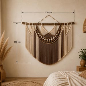 May include: A macrame wall hanging suspended from a wooden branch, featuring cream and brown cotton cords in a layered crescent design with decorative knots. The piece measures 120 cm in width and 110 cm in height, displaying a symmetrical pattern.