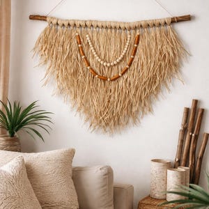 K&ouml;nnte beinhalten: Gro&szlig;e Wandbeh&auml;nge aus Naturfasern mit einem fransigen, dreieckigen Design. Es hat eine Holzstange und einen dekorativen Perlenakzent. Die neutralen T&ouml;ne und Texturen schaffen eine Boho-&Auml;sthetik, die sich f&uuml;r die Inneneinrichtung eignet.