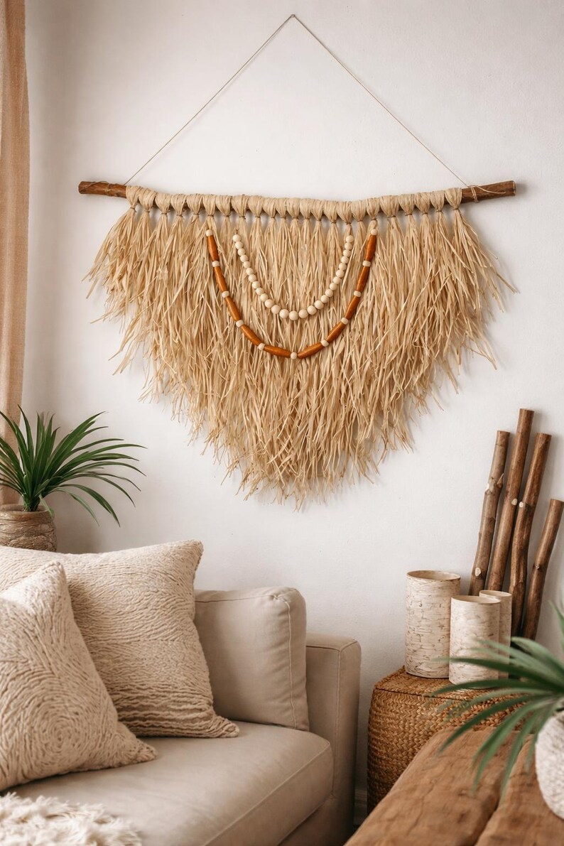 K&ouml;nnte beinhalten: Gro&szlig;e Wandbeh&auml;nge aus Naturfasern mit einem fransigen, dreieckigen Design. Es hat eine Holzstange und einen dekorativen Perlenakzent. Die neutralen T&ouml;ne und Texturen schaffen eine Boho-&Auml;sthetik, die sich f&uuml;r die Inneneinrichtung eignet.