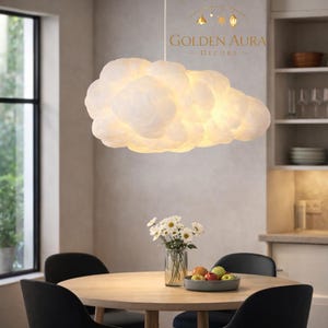 May include: A cloud-shaped pendant light fixture with a soft, glowing appearance. The fixture is white and hangs above a round wooden table. The text "GOLDEN AURA DECORS" is visible in the background.