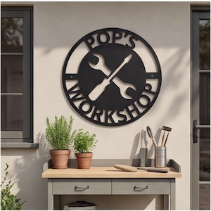 May include: A circular black metal wall sign featuring a cutout design of a wrench and a screwdriver crossed in the center. The text POP'S WORKSHOP is cut out along the top and bottom edges of the circular frame, creating a bold, industrial look.
