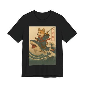 May include: Black t-shirt featuring a corgi riding a shark through ocean waves, with a sword in hand. The design includes Japanese text in a red box. The corgi is wearing a blue and red outfit.