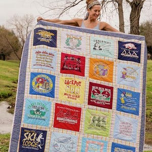 May include: A handmade quilt featuring squares of various colors and designs, including text and graphics from t-shirts. The quilt has a blue and white checkered pattern and a blue border. The quilt is held up by a person.