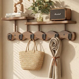 May include: A wooden wall shelf unit with hooks, displaying a woven tote bag and a rolled scarf. The shelf also holds a small speaker, books, and wooden bird ornaments. The unit is brown with black hooks.