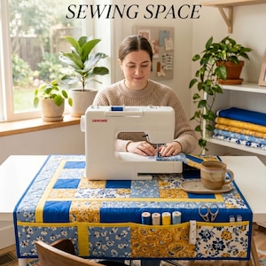 Puede incluir: Una mujer usa una máquina de coser Janome blanca sobre una mesa con un tapete de costura de retazos azul y amarillo. El tapete tiene bolsillos con carretes, tijeras y otros suministros de costura. El texto dice "Create Your Dream Sewing Space."