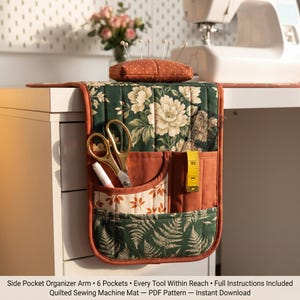 Puede incluir: Organizador lateral acolchado para máquina de coser con seis bolsillos. El organizador presenta un estampado floral en verde y crema, con detalles color óxido. Se ven tijeras doradas, una cinta métrica y un alfiletero.