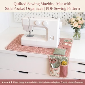 Op de afbeelding: Een witte naaimachine staat op een roze bloemen gewatteerde mat met een zijvak organizer. De organizer bevat een schaar, een pen en een meetlint. De tekst luidt "Quilted Sewing Machine Mat with Side Pocket Organizer | PDF Sewing Pattern."