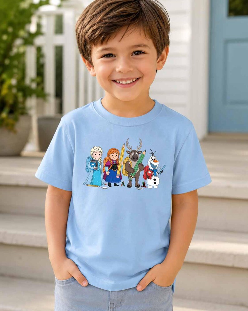 Puede incluir: Una camiseta de manga corta de color azul claro con un estampado gr&aacute;fico de cuatro personajes de dibujos animados de Frozen, incluidos Elsa, Anna, Sven y Olaf, todos representados con material escolar como mochilas, l&aacute;pices y libros.