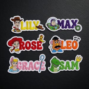 May include: Embroidered patches featuring characters and names from the Toy Story franchise. The patches include characters like Woody, Buzz Lightyear, Jessie, Mr. Potato Head, and Rex, with names such as Lily, Max, Rose, Leo, Grace, and Sam.