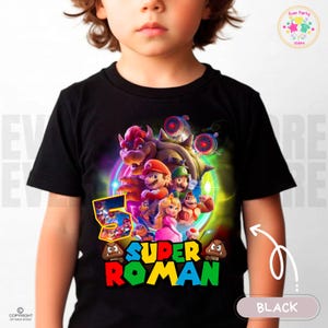 Puede incluir: Camiseta negra con un diseño colorido de personajes de Super Mario, incluyendo a Mario y Peach. El diseño incluye el texto "SUPER ROMAN" y el número "5". Prenda de vestir para niños.