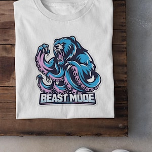 May include: White t-shirt featuring a blue bear with pink tentacles and the text "BEAST MODE" in a rectangular box. The shirt is folded on a wooden surface, with white sneakers visible below.