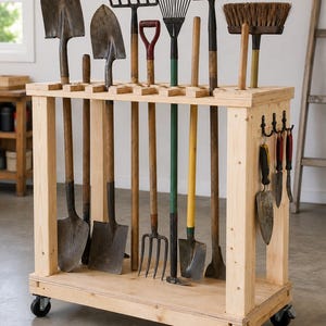 May include: A light-coloured wooden garden tool organiser on four black caster wheels. The rectangular rack features slots along the top for long-handled tools like shovels, rakes, and a broom, with three small metal hooks on the side for hand tools.