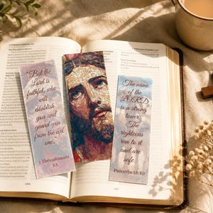 Puede incluir: Un libro abierto con tres marcadores con citas e imágenes religiosas. Una cruz de madera y una taza de café están cerca. Los marcadores tienen texto de la Biblia, incluyendo "Pero el Señor es fiel" y "El nombre del Señor es una torre fuerte."