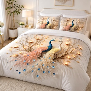 Puede incluir: Un juego de cama blanco con un diseño estampado de dos pavos reales, uno azul y otro blanco, rodeados de ramas doradas y velas de té brillantes. El patrón se repite en la funda nórdica y en las dos fundas de almohada rectangulares a juego.