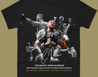 Puede incluir: Camiseta negra con un collage de imágenes de Conor McGregor, incluyendo cinturones de campeonato. El texto dice "NOTORIOUS" CONOR MCGREGOR y detalla sus victorias en la UFC. Un diseño para fans.