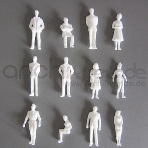 Op de afbeelding: Een verzameling kleine, witte architectuurfiguren in verschillende poses, waaronder staan, zitten en armen over elkaar. De figuren zijn uniform gekleurd en lijken van plastic te zijn. De achtergrond is effen grijs.