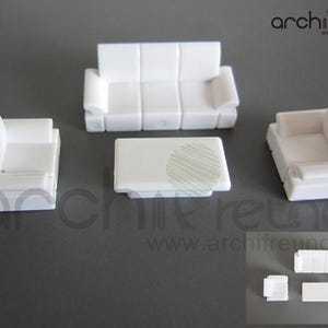 Può includere: Un set di mobili bianchi in miniatura, composto da un divano a tre posti, due poltrone e un tavolino rettangolare. Il set è realizzato in un materiale solido e opaco, con un design moderno e squadrato. Il sito web "www.archifreunde.de" è visibile.