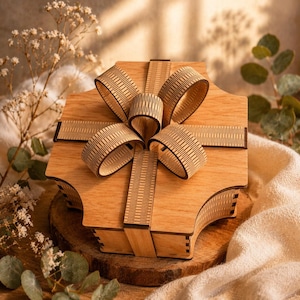 May include: A wooden gift box with a decorative bow. The box is light brown with a detailed bow design. The bow has a textured pattern. The box is sitting on a wooden surface.