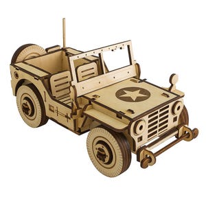 Può includere: Un modello in legno di una jeep in stile militare. Il modello è realizzato in legno chiaro con bordi marroni più scuri. Il cofano presenta un'emblema a stella. La jeep ha una ruota di scorta, sedili e un parabrezza.