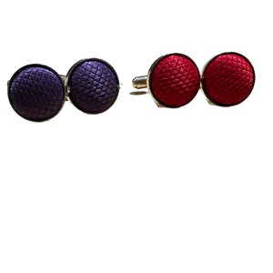 May include: A pair of cufflinks, one with a purple fabric button and the other with a red fabric button.