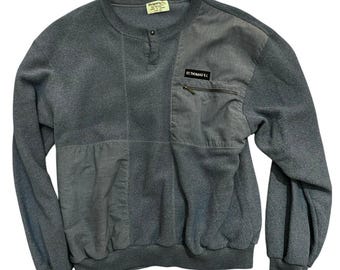 May include: A gray sweatshirt with a patchwork design. The sweatshirt features a quarter-zip neckline, a small pocket with a zipper, and the text "ST. THOMAS N.I." on the pocket. The cuffs and hem are ribbed.