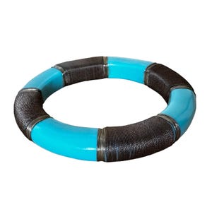 Puede incluir: Un brazalete de color turquesa y marrón con detalles plateados. El brazalete está hecho de un material liso y duro y tiene una forma circular.