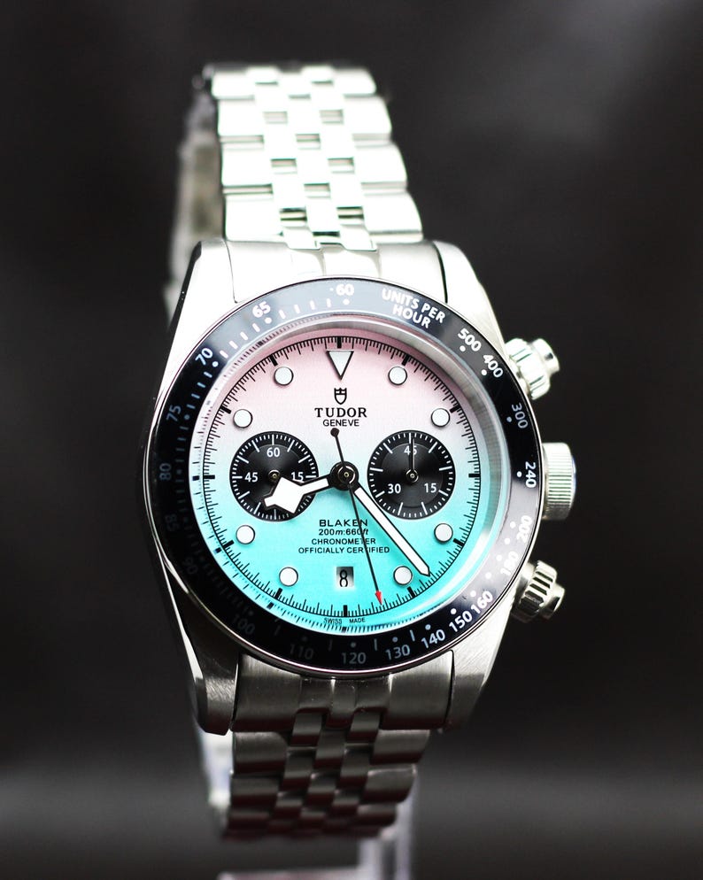 Puede incluir: Un reloj cron&oacute;grafo Tudor de acero inoxidable con una esfera degradada que pasa de blanco en la parte superior a turquesa en la inferior. Cuenta con un bisel taquim&eacute;trico negro, dos subesferas negras, una ventana de fecha a las seis y un brazalete de eslabones met&aacute;licos.