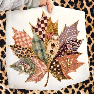 Peut inclure: Une grande impression graphique en forme de feuille d'érable avec un motif patchwork composé de carreaux, d'imprimé léopard, de pois et de fleurs. Le motif inclut des illustrations de citrouilles, de glands, de champignons et d'épis de blé dorés.