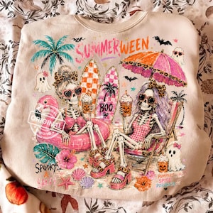 May include: Beige sweatshirt with a colorful "Summerween" graphic. Two skeleton figures are enjoying a beach scene with surfboards, ghosts, and palm trees. One skeleton is in a pink flamingo float, and the other is in a beach chair. The words "Spooky" and "Pumpkin Spice Paradise" are also visible.