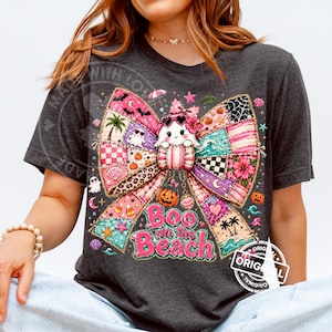 May include: Dark gray t-shirt featuring a colorful patchwork bow design with a cute ghost wearing sunglasses. The text "Boo on the Beach" is displayed in pink. Halloween-themed apparel.