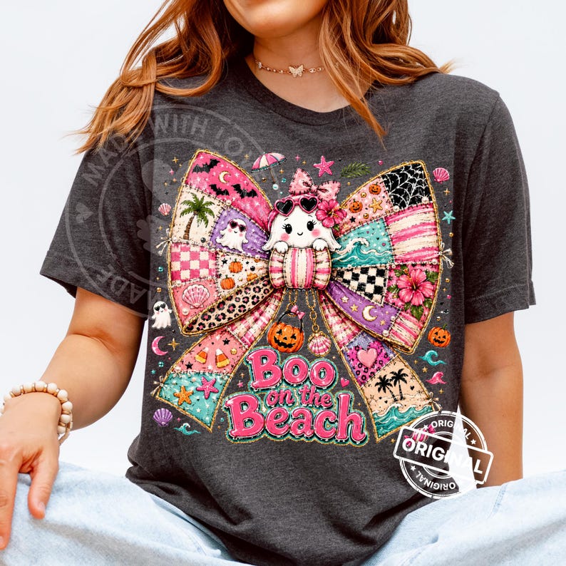 May include: Dark gray t-shirt featuring a colorful patchwork bow design with a cute ghost wearing sunglasses. The text "Boo on the Beach" is displayed in pink. Halloween-themed apparel.