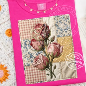 May include: A bright pink t-shirt with a patchwork design of roses. The roses are made of various patterned fabrics, including floral and gingham prints. The shirt has a Comfort Colors tag and a delicate necklace.