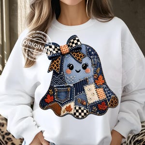 May include: A white long-sleeve sweatshirt featuring a central graphic of a ghost made of various denim and fabric patches. The ghost has a large bow, embroidered maple leaves, acorns, and a small pocket detail, all in a patchwork style.