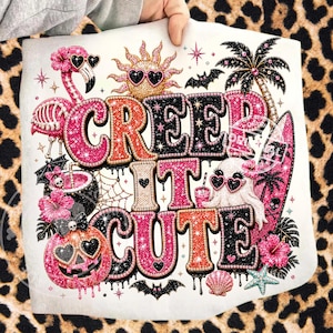 May include: A white tote bag featuring the phrase "Creep It Cute" in a sparkly, colourful design. The design includes a flamingo, sun, palm tree, pumpkin, and ghost, all wearing heart-shaped sunglasses. The background is a leopard print.