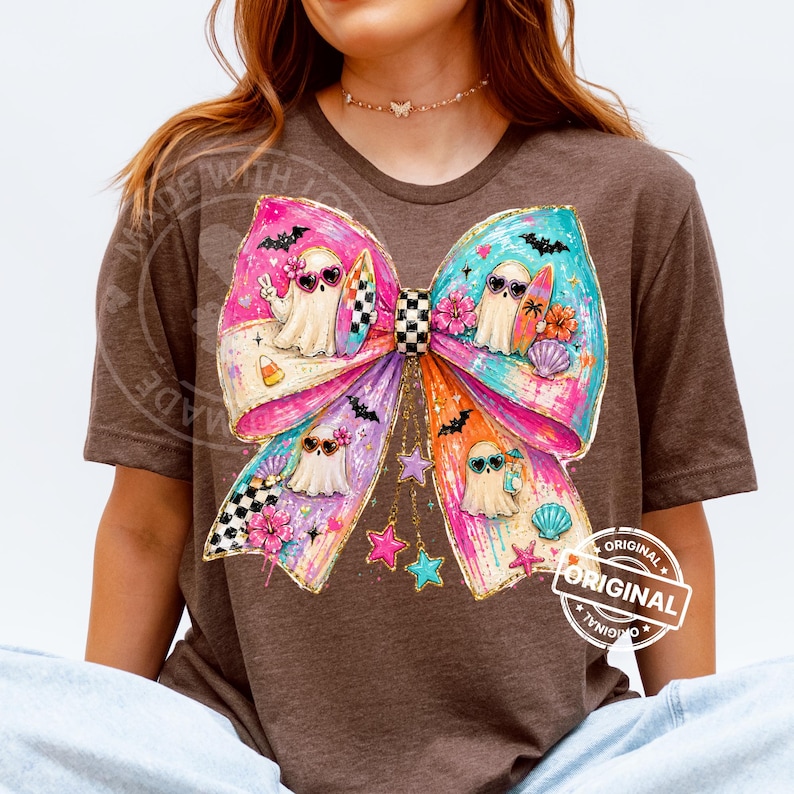 Pu&ograve; includere: T-shirt marrone con un grande fiocco colorato con personaggi fantasma con occhiali da sole. Il fiocco presenta sezioni rosa, viola, blu e gialle con stelle, pipistrelli e conchiglie. Il testo "ORIGINAL" &egrave; stampato sulla maglietta.