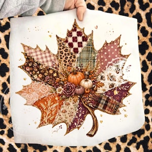 May include: A large maple leaf graphic print featuring a patchwork design of various patterns including plaid, leopard print, floral, and lace in shades of brown, orange, and cream. The center is decorated with small pumpkins and berries.