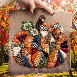 May include: A fabric pumpkin decoration featuring a patchwork design with various patterns including leopard print, gingham, floral, and plaid in orange, green, blue, and brown. It includes two quilted green leaves and a decorative bow on top.